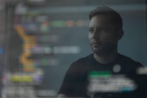 Zu sehen ist die Spiegelung eines Mannes auf einem Bildschirm. Er bietet IT-Services trotz Corona. Bild: Unsplash/Peter G
